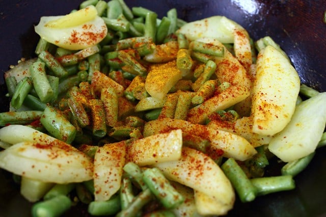 ground spices added on sautéed french beans and potatoes