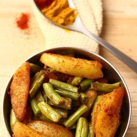 aloo beans recipe served in a steel bowl on a cream colored cotton woven napkin.