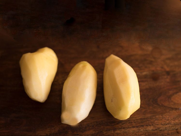 three peeled potatoes on a wooden board