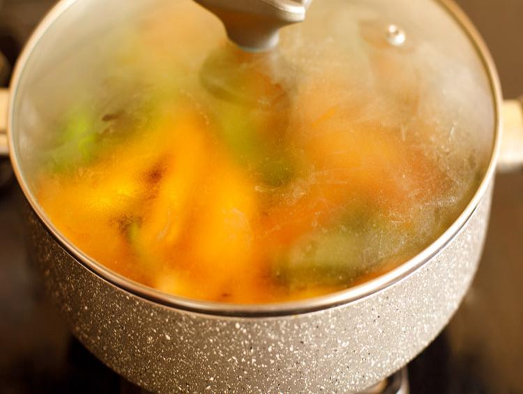 cooking aloo capsicum with a glass lid on the pan