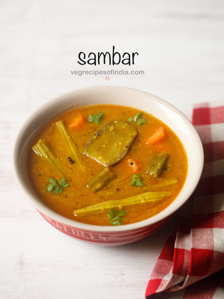 sambar served in a cream bowl on a white board with a red & white checkered napkin on the side