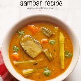 sambar served in a cream bowl on a white board with a red & white checkered napkin on the side