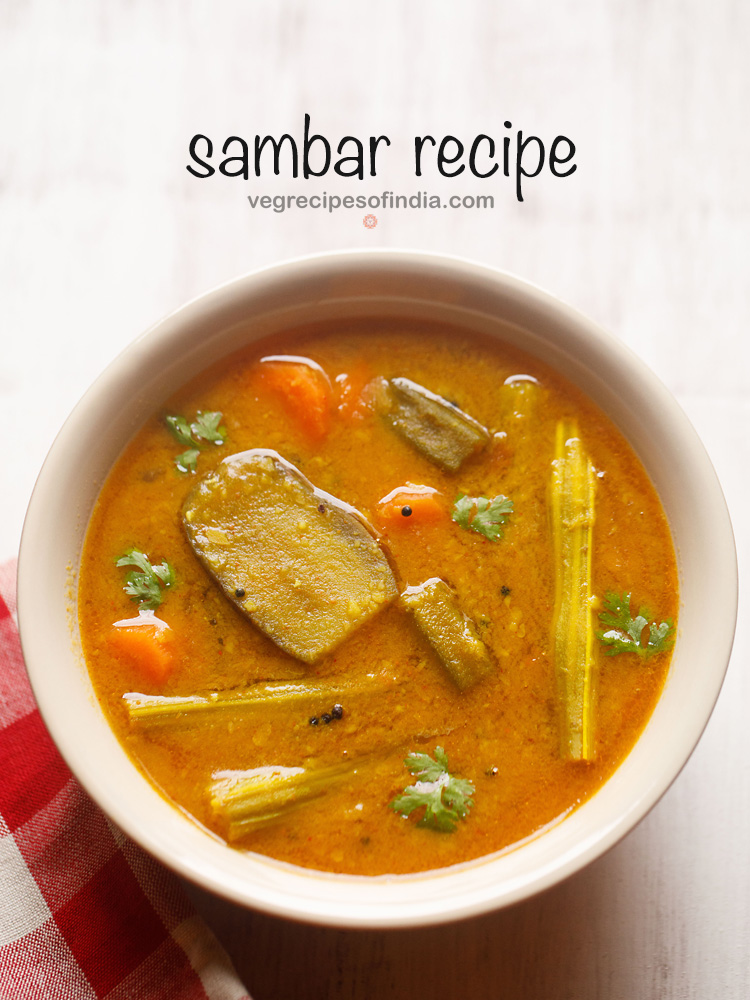 sambar served in a cream bowl on a white board with a red & white checkered napkin on the side