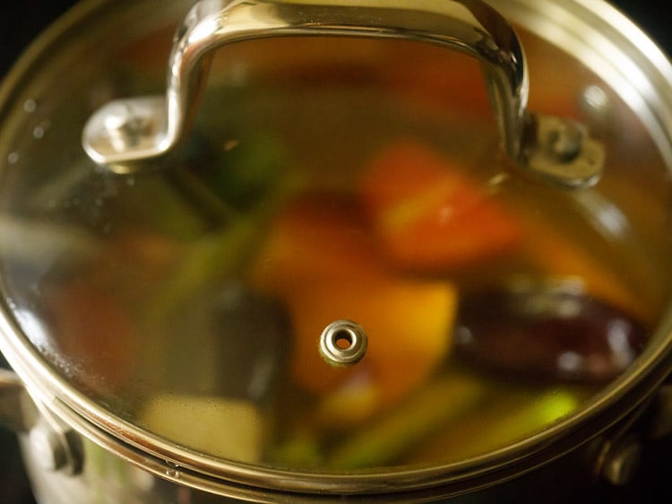 pot covered with a glass lid and veggies being cooked