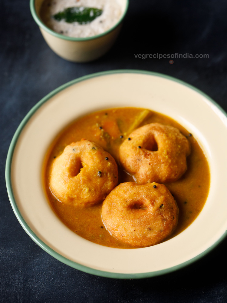 medu vada dunked in sambar in a cream plate on a dark navy blue board
