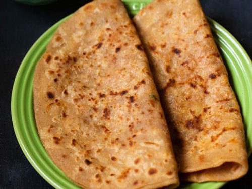 aloo paratha folded and placed on a green ceramic plate on a dark bluish board, side of butter cubes.