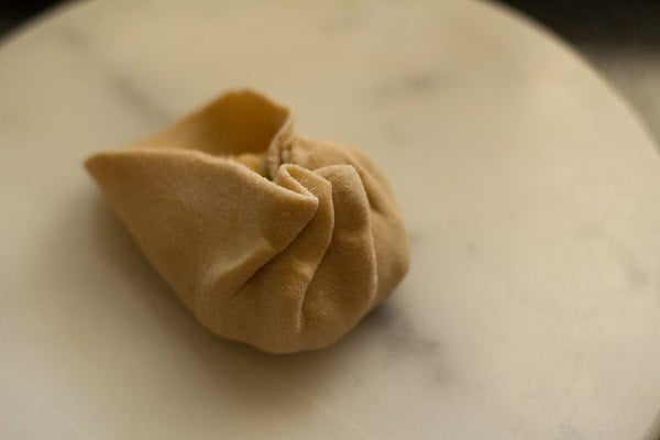 folding and pleating the paratha dough to shut it around the aloo filling.