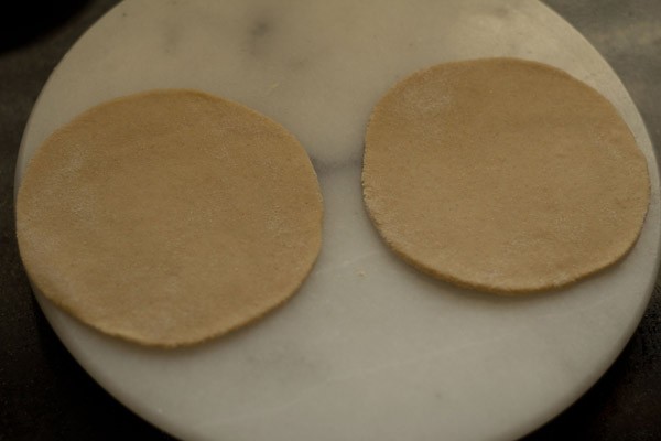 two discs of paratha dough on a marble slab.