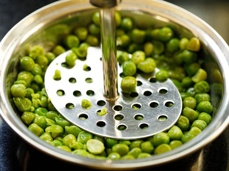 drained steamed peas being mashed in a bowl.