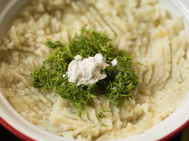 adding coriander leaves and salt to mashed potatoes in the bowl