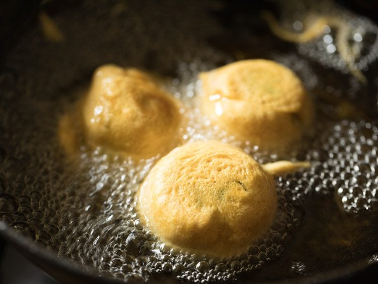 frying and turning batata vada in hot oil