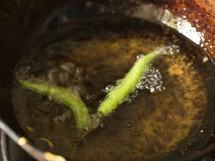 frying slit green chillies in hot oil till faint golden