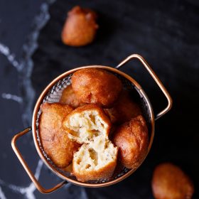 top shot of one gulgule or pua showing its soft and porous texture with the remaining gulgule placed in a netted copper frying bucket