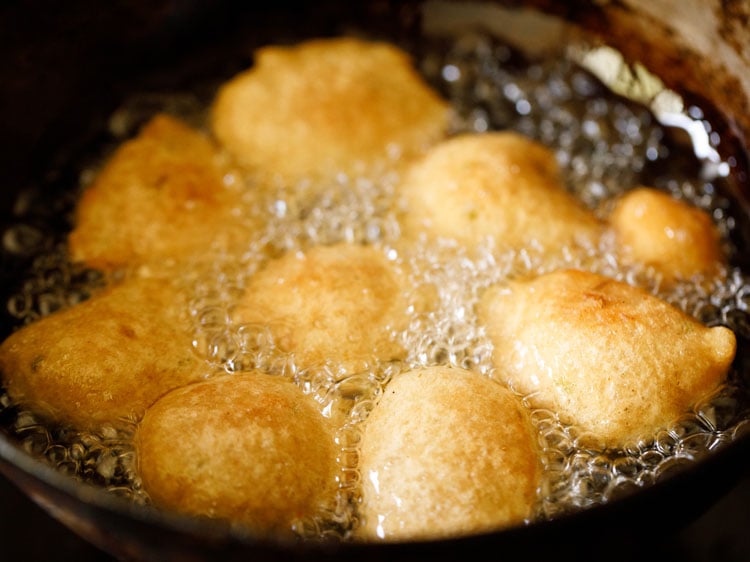 gulgule being fried are becoming golden and puffed.