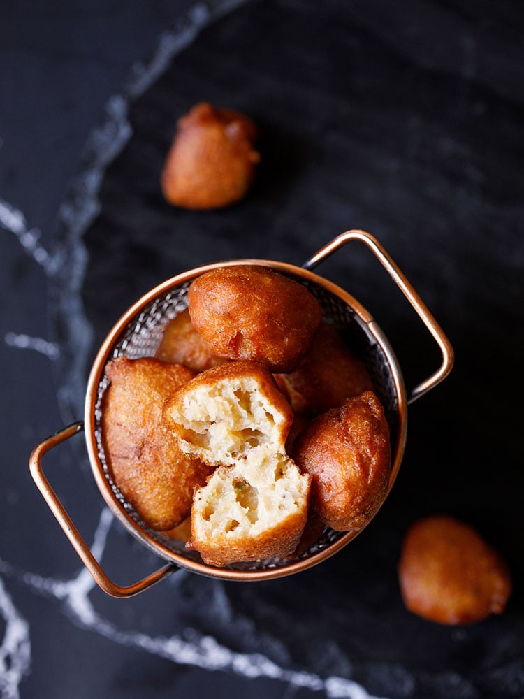 top shot of one gulgule or pua showing its soft and porous texture with the remaining gulgule placed in a netted copper frying bucket