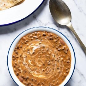 instant pot dal makhani served in a navy blue rimmed white glass bowl with a brass spoon on the side on a white marble board