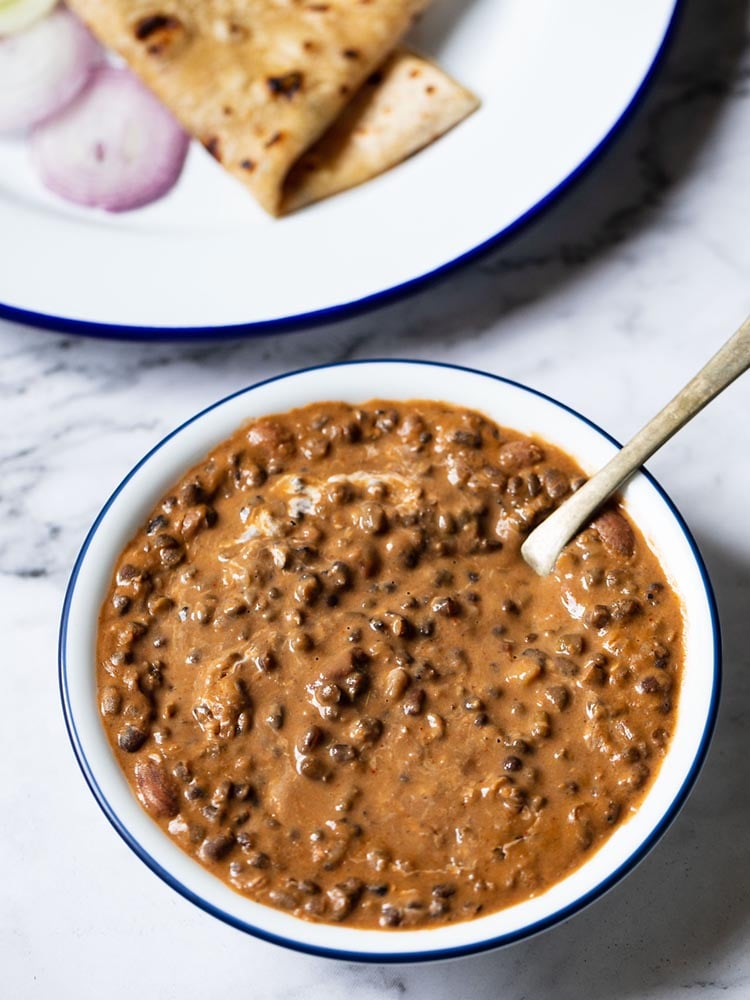 instant pot dal makhani served in a navy blue rimmed white glass bowl with a brass spoon inside the bowl. kept on a white marble board. 