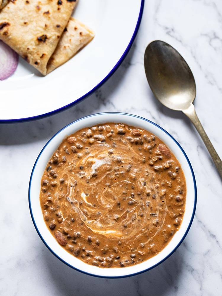 instant pot dal makhani served in a navy blue rimmed white glass bowl with a brass spoon on the side on a white marble board. 