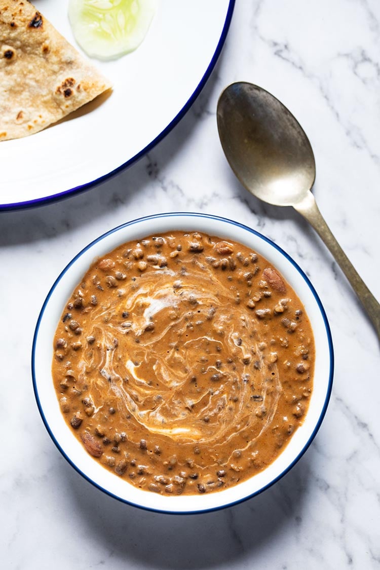 instant pot dal makhani served in a navy blue rimmed white glass bowl with a brass spoon on the side on a white marble board