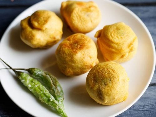 batata vada served on a white plate with fried green chilies kept on the left side.