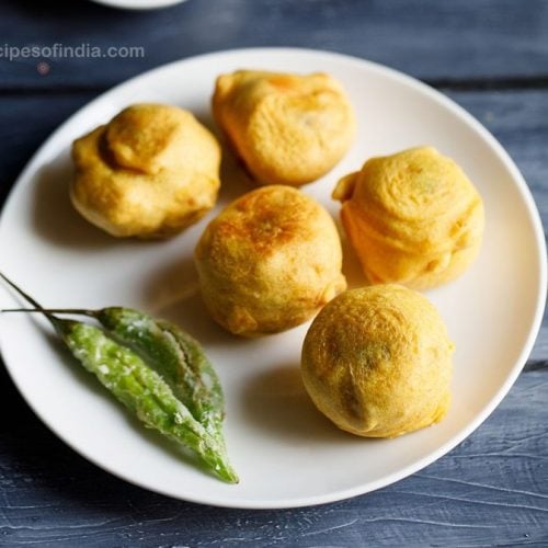 batata vada served on a white plate with fried green chilies kept on the left side.