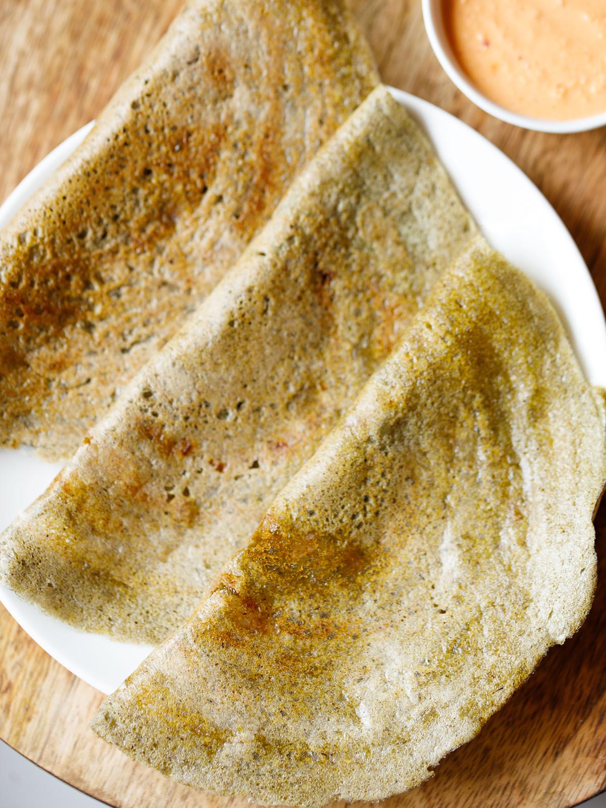 three pesarattu or moong dal dosa folded and kept on a white plate with a orange colored coconut chutney in a side bowl