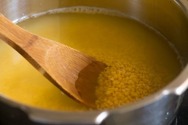 moong lentils and water being stirred in pressure cooker