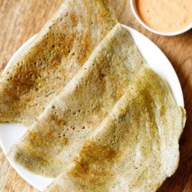 three pesarattu or moong dal dosa folded and kept on a white plate with a orange colored coconut chutney in a side bowl