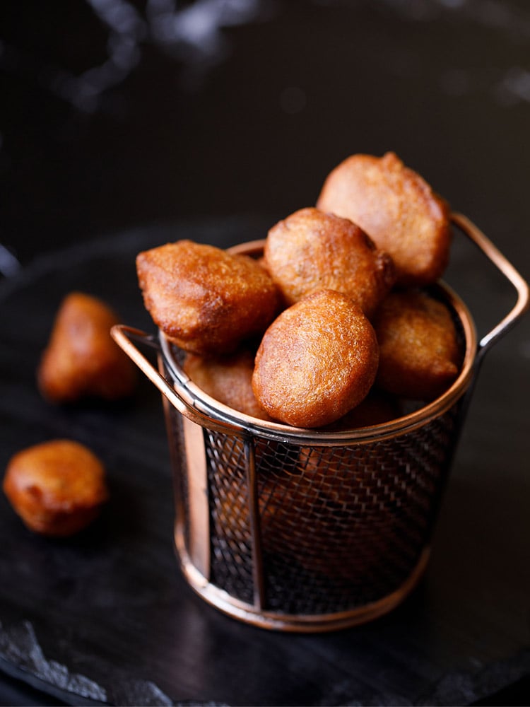 pua or gulgule placed in a netted copper frying bucket on a black board.