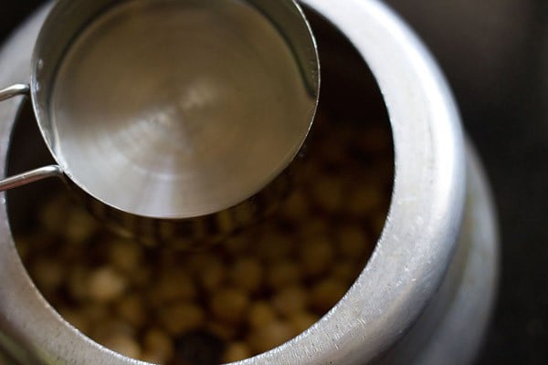 measuring cup with water above a pressure cooker filled with chickpeas