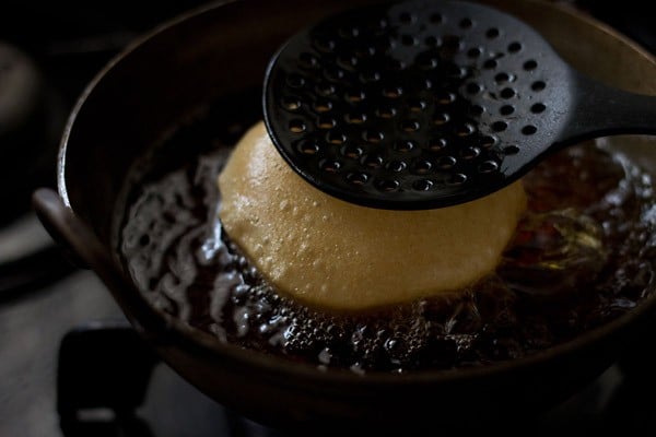 pressing poori with spoon to help it cook.