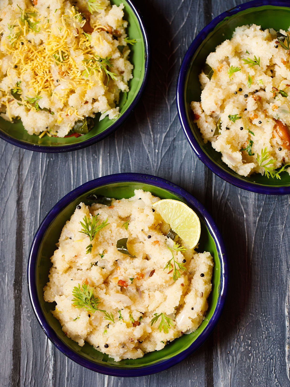 upma garnished with cilantro and a lemon wedge served in a dark green blue rimmed plate on a dark blue wooden board