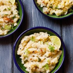 upma garnished with cilantro and a lemon wedge served in a dark green blue rimmed plate on a dark blue wooden board