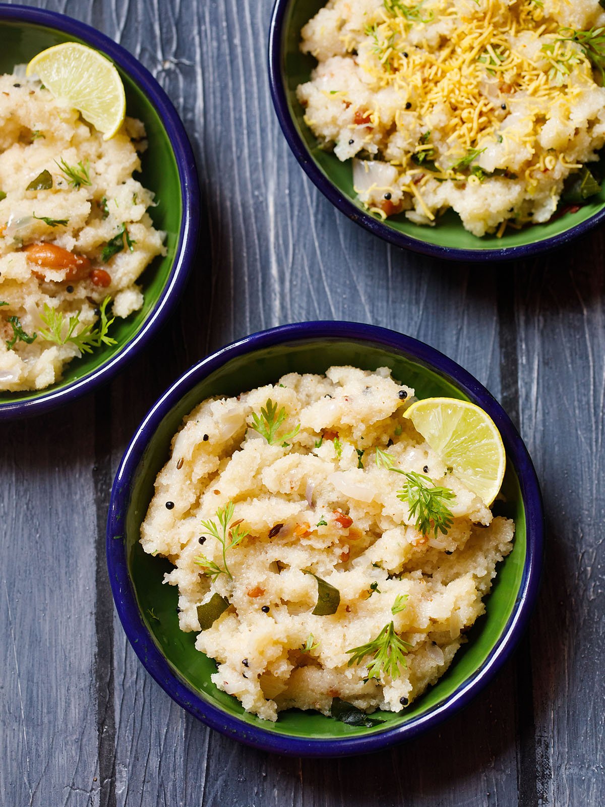 upma garnished with cilantro and a lemon wedge served in a dark green blue rimmed plate on a dark blue wooden board