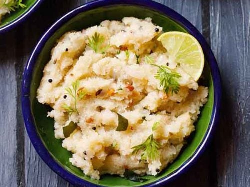 upma garnished with cilantro and a lemon wedge served in a dark green blue rimmed plate on a dark blue wooden board