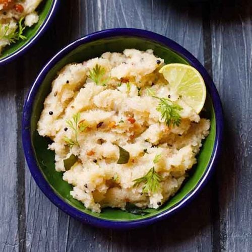 upma garnished with cilantro and a lemon wedge served in a dark green blue rimmed plate on a dark blue wooden board