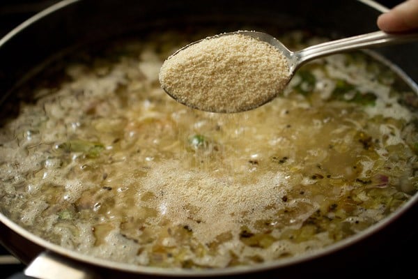 adding rava with a spoon to make upma recipe