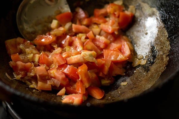 sauteing tomatoes in a pan with onions