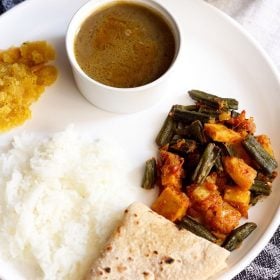 aloo bhindi served on a white plate with roti, steamed rice and dal.