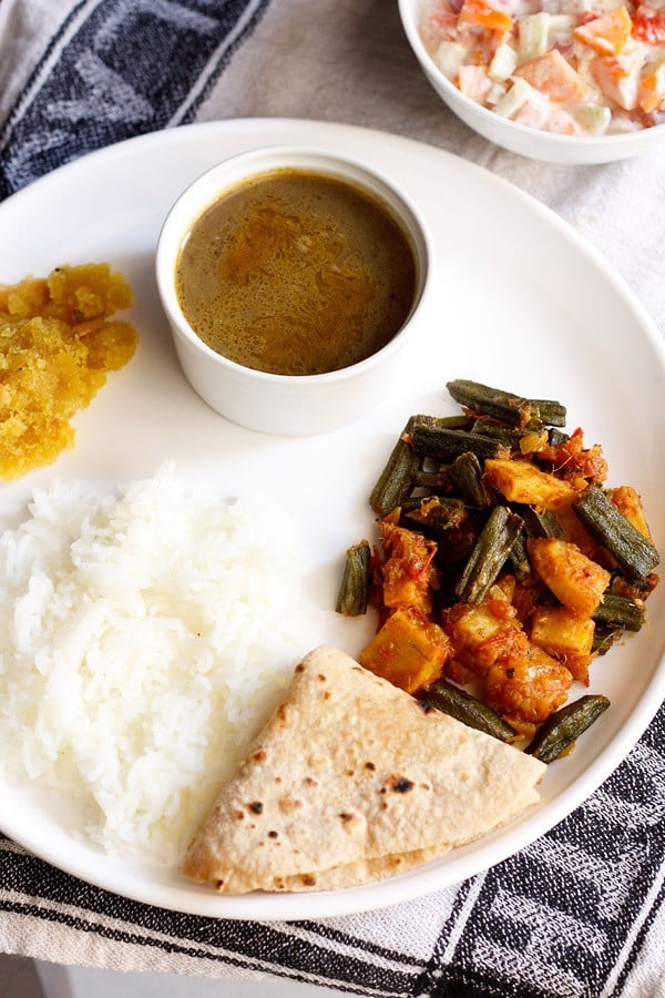 aloo bhindi served on a white plate with roti, steamed rice and dal.