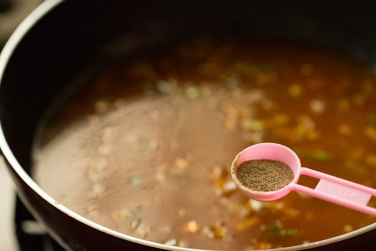 black pepper powder being added with a pink measuring spoon