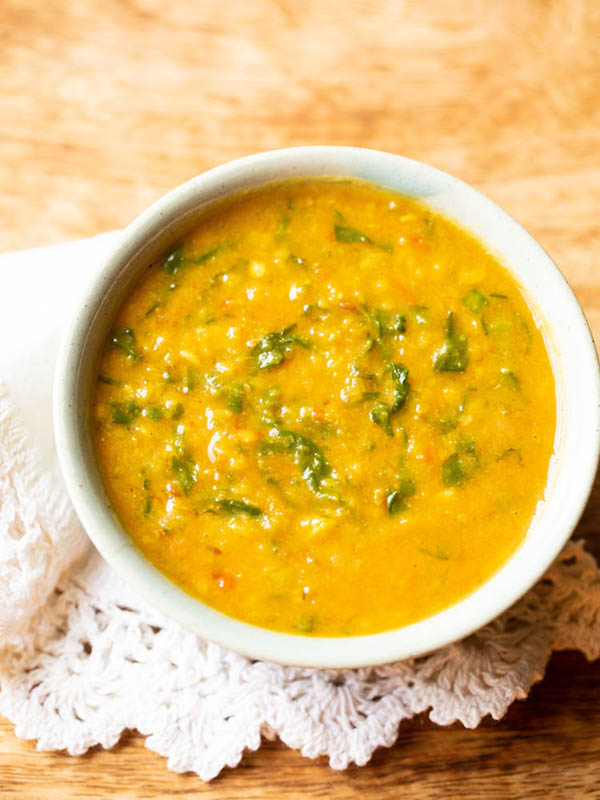 instant pot palak dal in a light aqua green bowl placed on a white crocheted napkin on a brown-beige wooden board