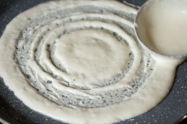 spreading dosa batter on the skillet