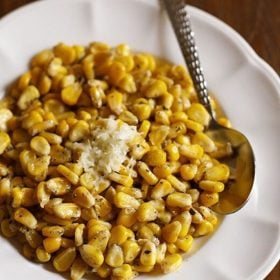 buttered corn served on a white plate with a silver spoon.
