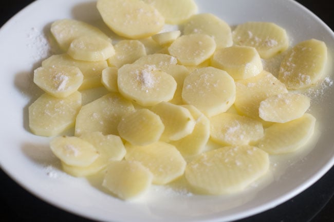 salt added to sliced potatoes in a plate