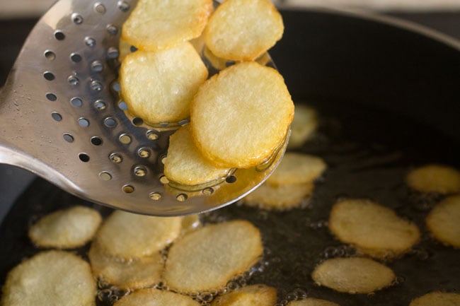 fried potato slices removed with a slotted spoon