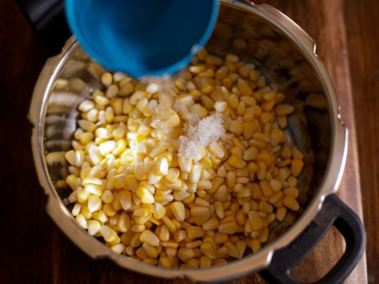 Add the rinsed corn kernels in a pressure cooker with salt and water