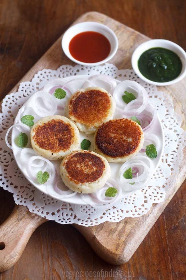 paneer patties served on a white plate with sliced onions with chutney as a side