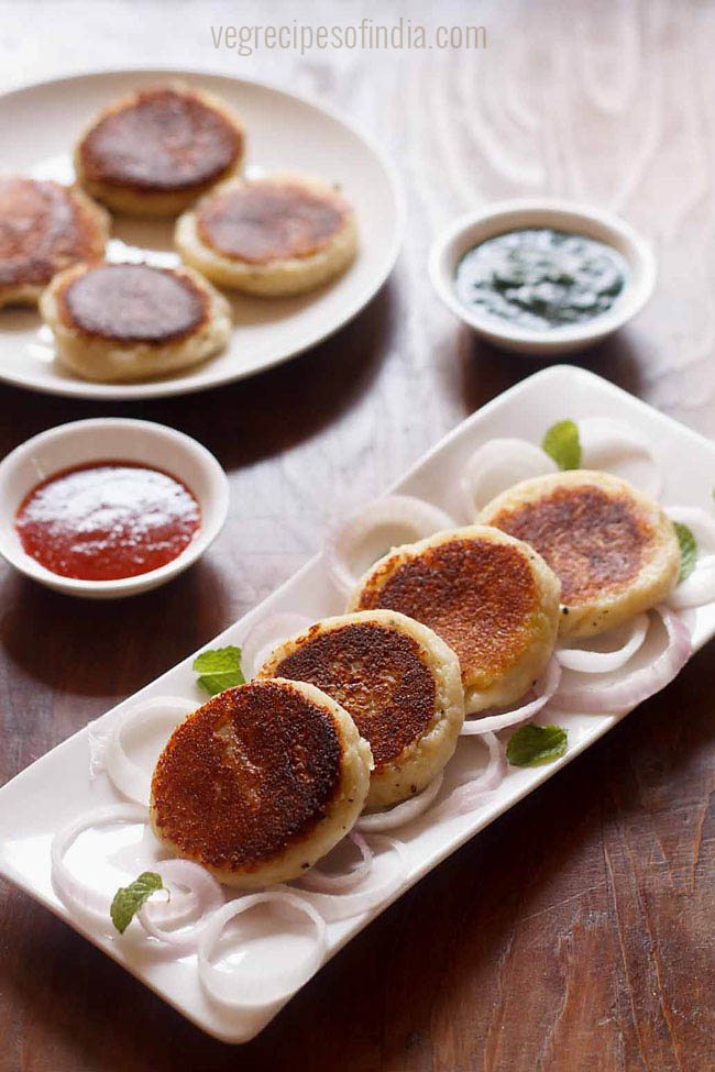 paneer patties served on a white plate on a bed sliced onions with chutney as a side