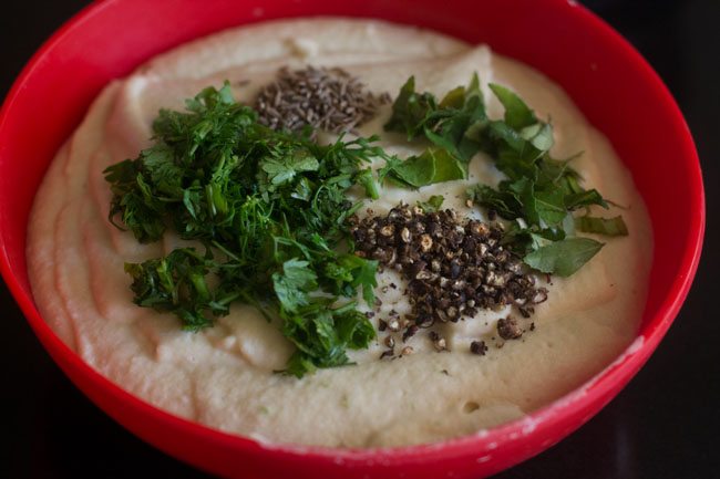 cumin seeds, crushed black peppercorns, chopped curry leaves and chopped coriander leaves added to ground lentil paste. 